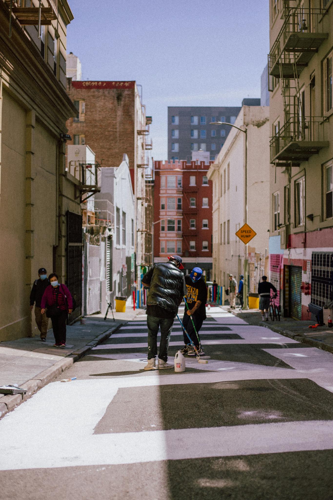 People painting in a vibrant urban alleyway during the day, showcasing street art creation.
